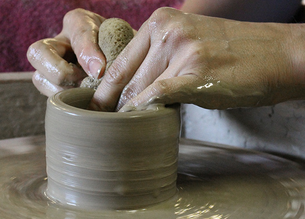Hands making clay vessel on pottery wheel