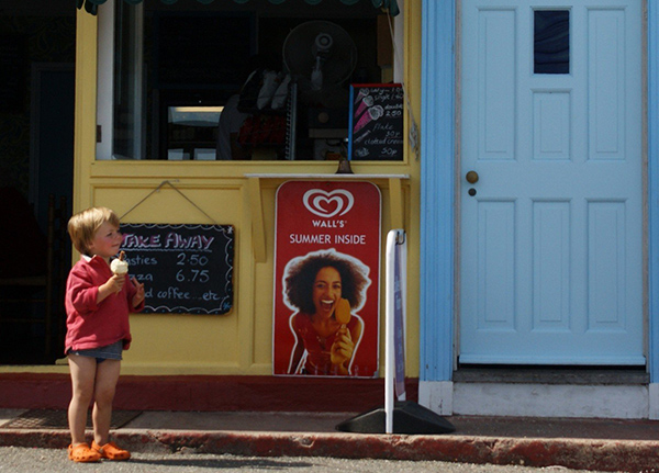 Small child with ice cream cone in front of small business stand