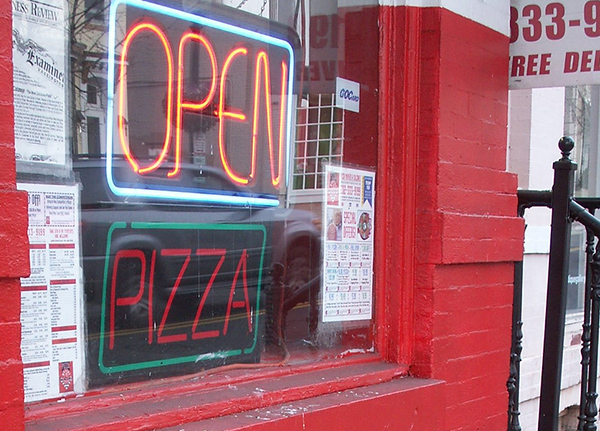 Open sign in the window with a neon sign that says pizza