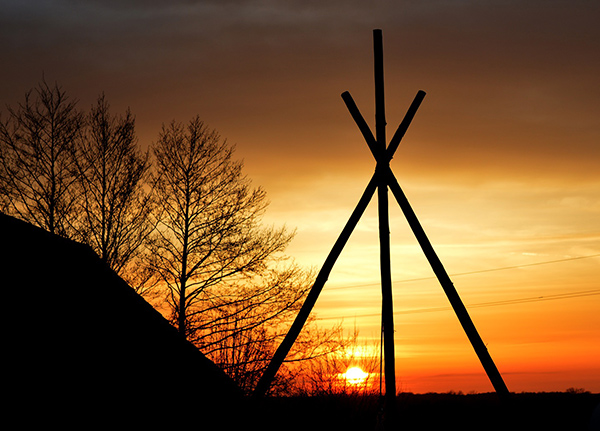 Silhouette of a teepee frame with a sunset in the background