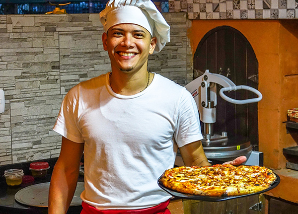 Man wearing chef's hat holds pizza and smiles
