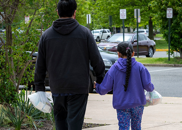 Man and daughter hold hands and carry grocery bags