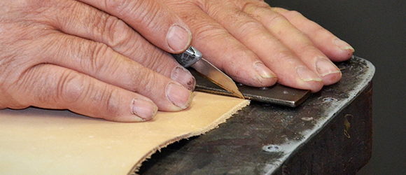 Hands holding Exacto knife and cutting through leather