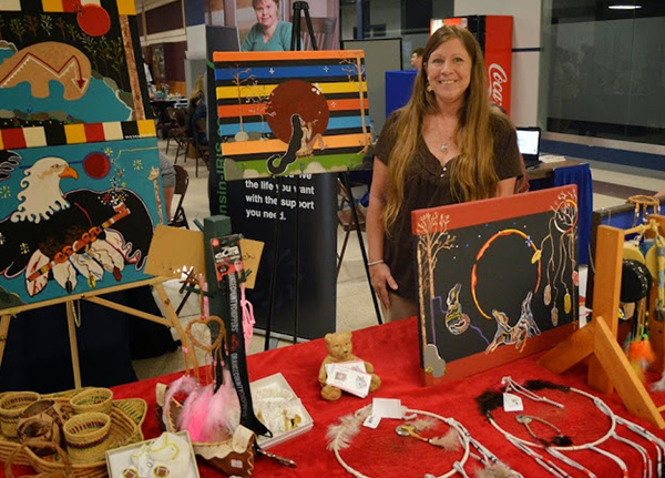 Woman smiles behind artwork at a craft fair booth