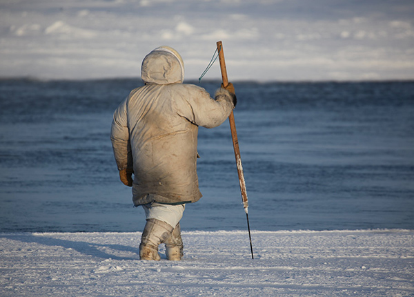 Person wearing warm winter clothing walks across the ice with a spear in their hand