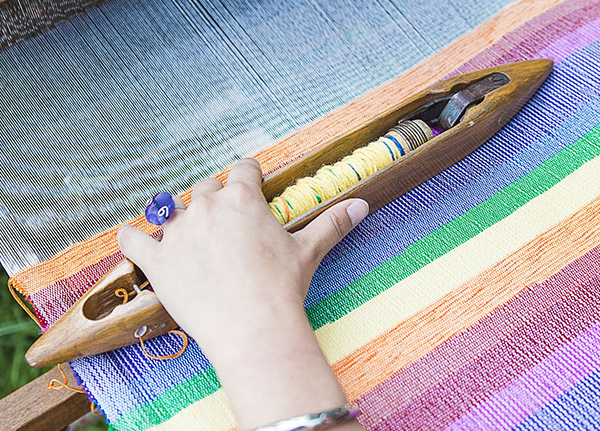 Hands using loom to weave fabric