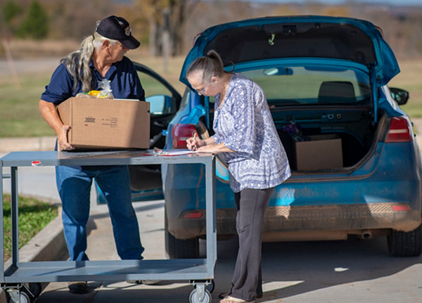 Man helps woman load a box into the trunk of car