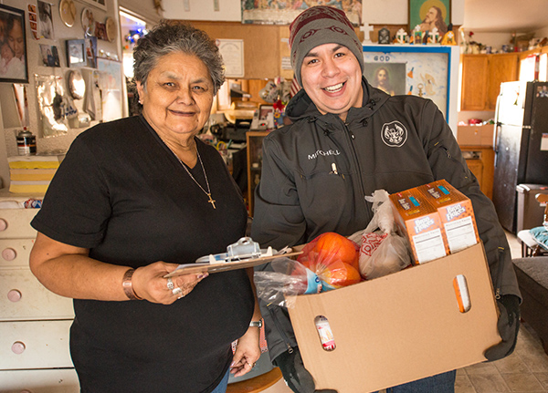 Woman holding a clipboard and man holding a box of food stand next to each other smiling