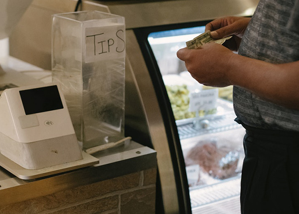 Person holding a dollar bill at a checkout counter