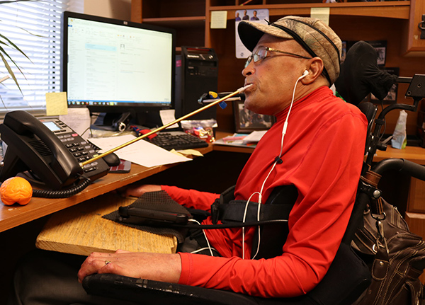 Man in wheelchair uses a mouth stick to make a phone call