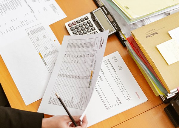 Person holding a paper spreadsheet with a calculator and other files in the background