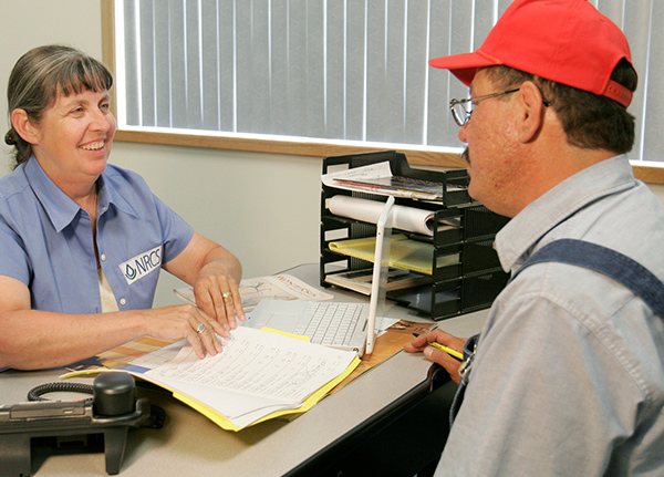 Client sits across from woman at a desk who is going through paperwork