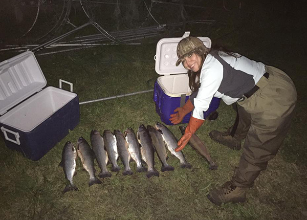 Woman crouches by nine freshly caught fish